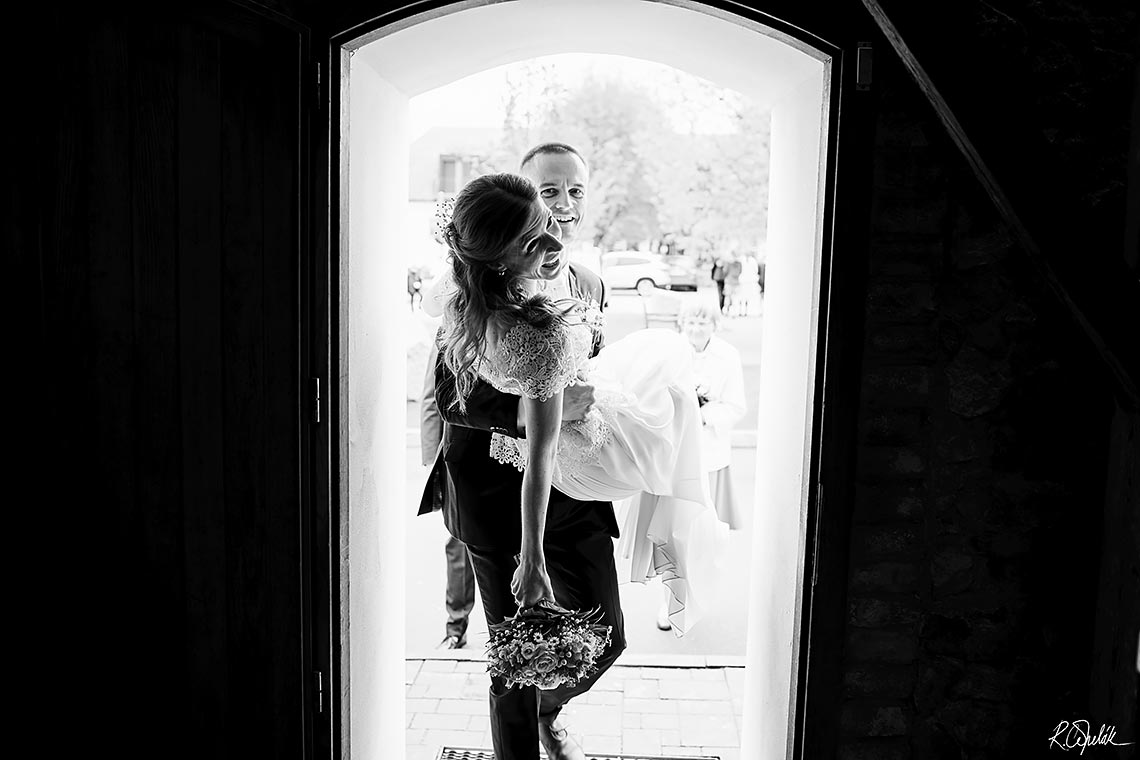 groom holding her bride in hands crossing doorsill