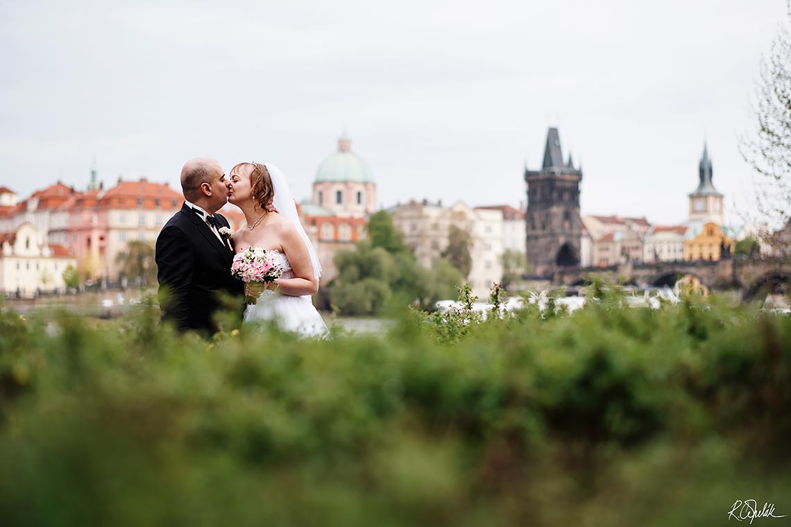 kissing bride and groom with Prague at background