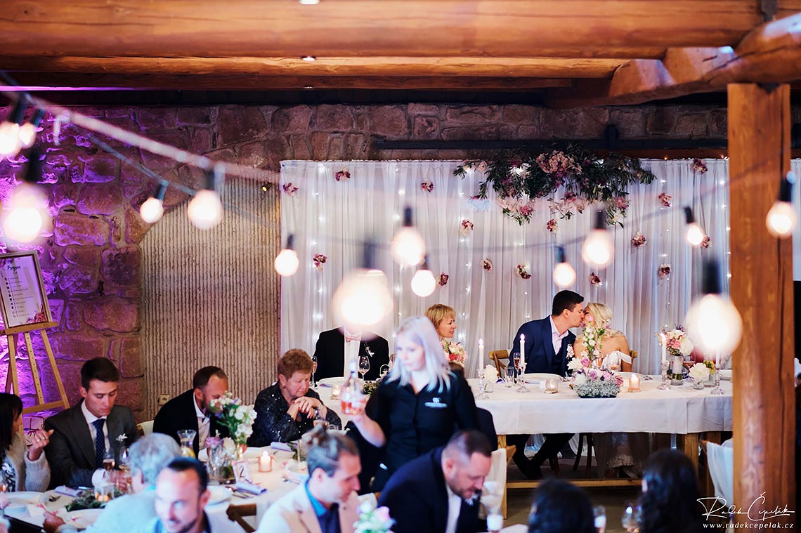 Bride and groom kissing each other at wedding reception with bulbs.