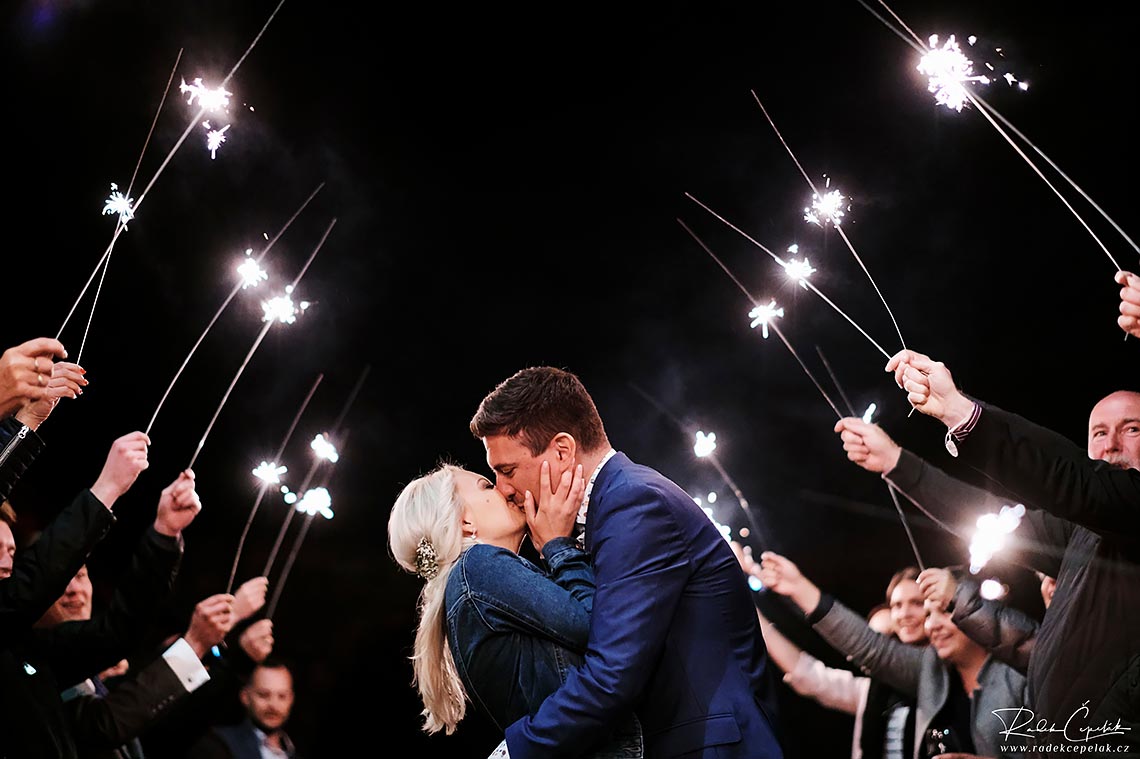 Romantic sweet kiss of bride and groom under sparkles in the evening at wedding in Hejtmankovice barn