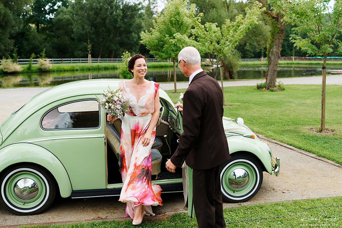 Bride getting off VW Beatle to outside wedding ceremony